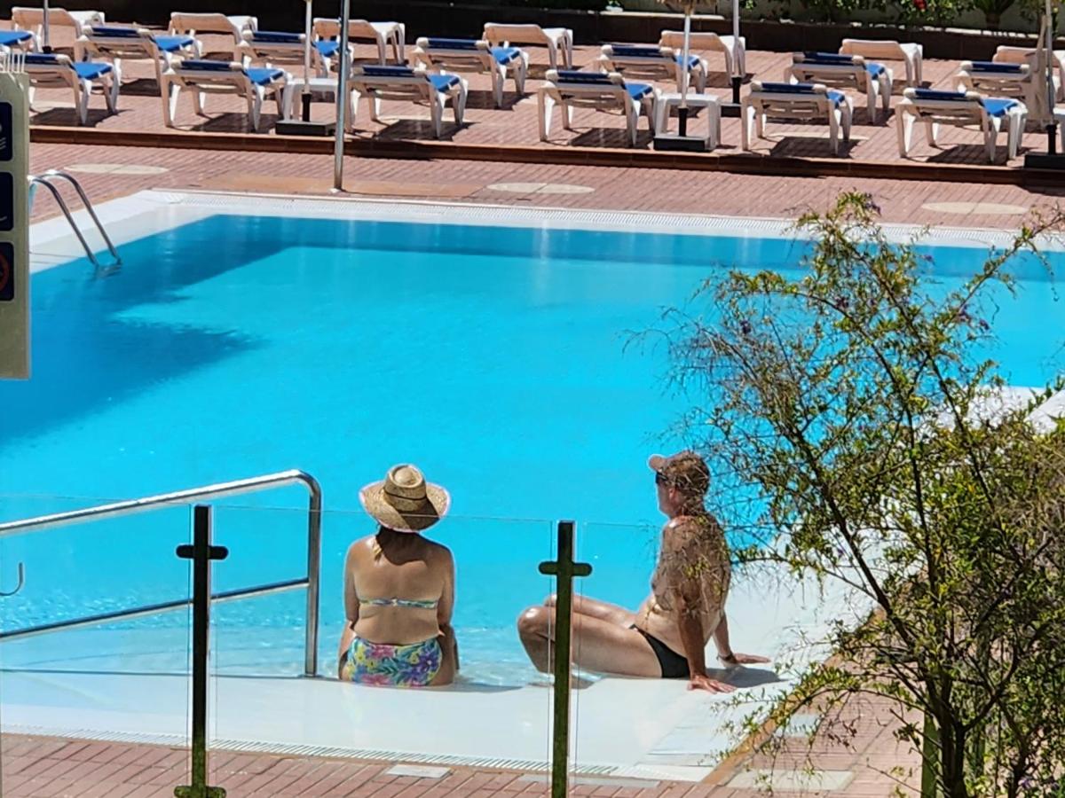 twee mensen zitten naast een zwembad bij Las Camelias Apartments in Playa del Inglés
