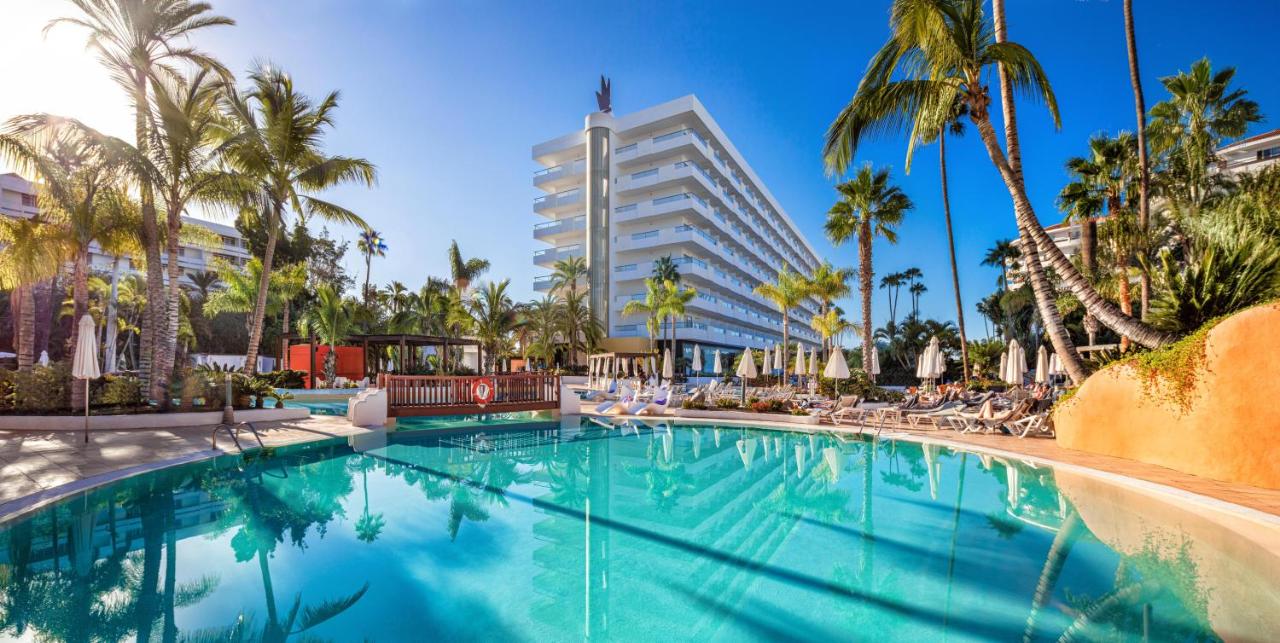 een zwembad met palmbomen en een hoog gebouw bij Hotel Gran Canaria Princess - Adults Only in Playa del Inglés