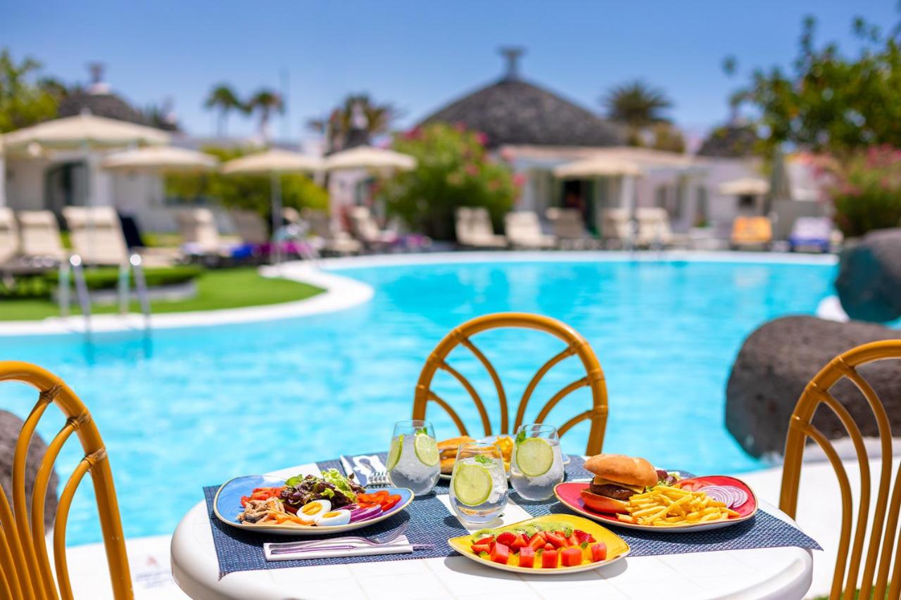 een tafel met borden eten naast een zwembad bij MUR Bungalows Parque Romantico in Playa del Inglés