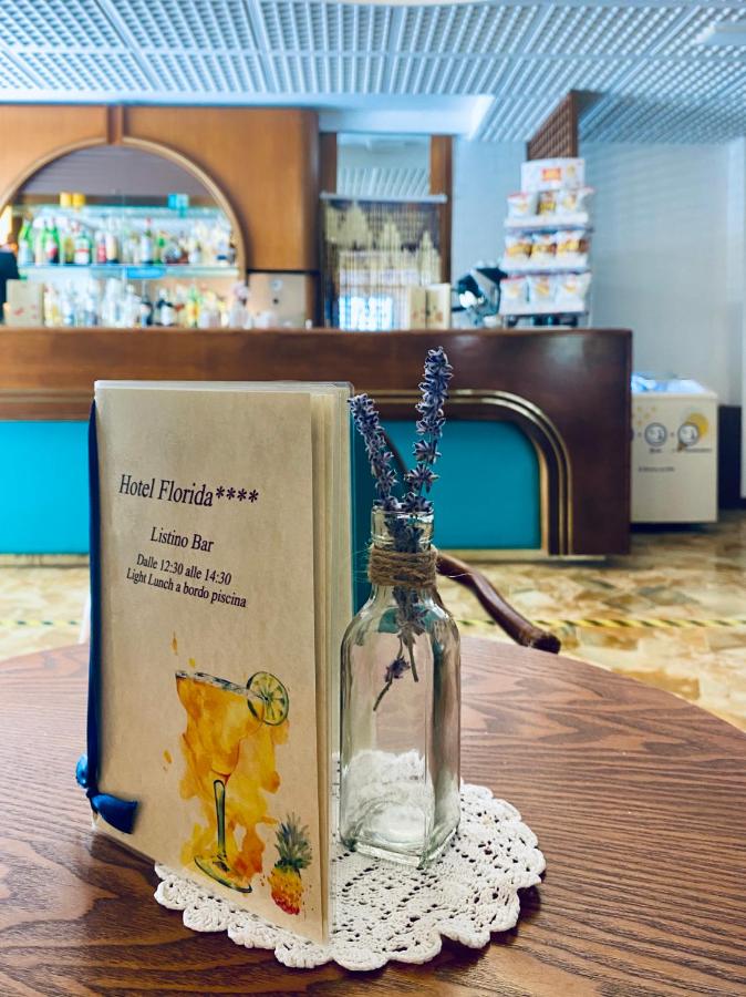 een boek en een fles met een bloem erin op een tafel bij Hotel Florida in Lido di Jesolo