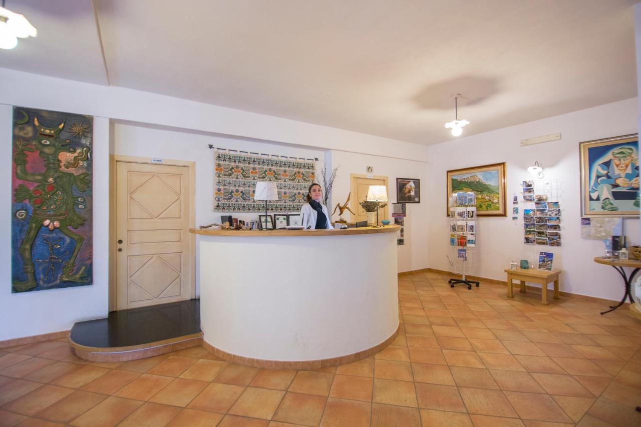 een vrouw die achter een toonbank staat in een kamer met schilderijen bij Gorropu Hotel in Urzulei