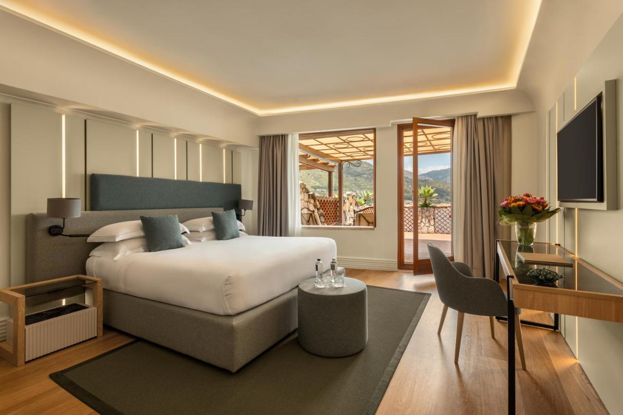 een slaapkamer met een bed, een tafel en een bureau bij Atlantis Bay - The Leading Hotels of the World in Taormina