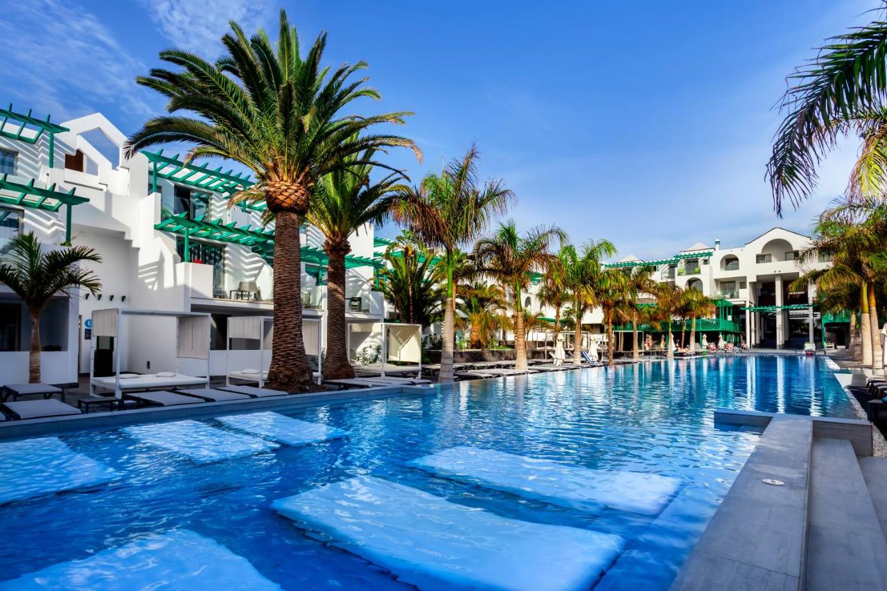 een groot zwembad met palmbomen en gebouwen bij Barceló Teguise Beach - Adults Only in Costa Teguise