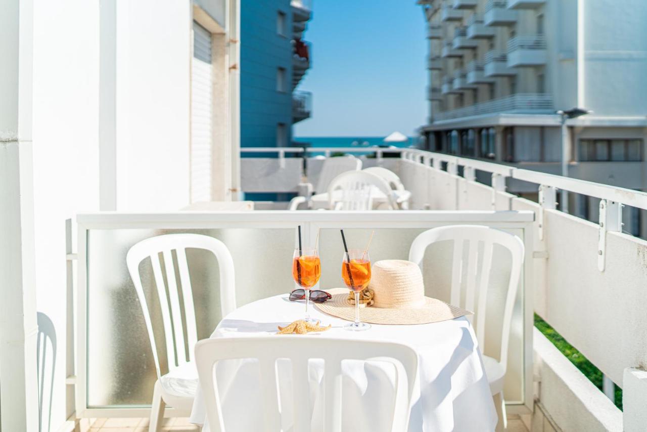 een witte tafel met twee glazen en een hoed op een balkon bij Hotel Pigalle in Lido di Jesolo
