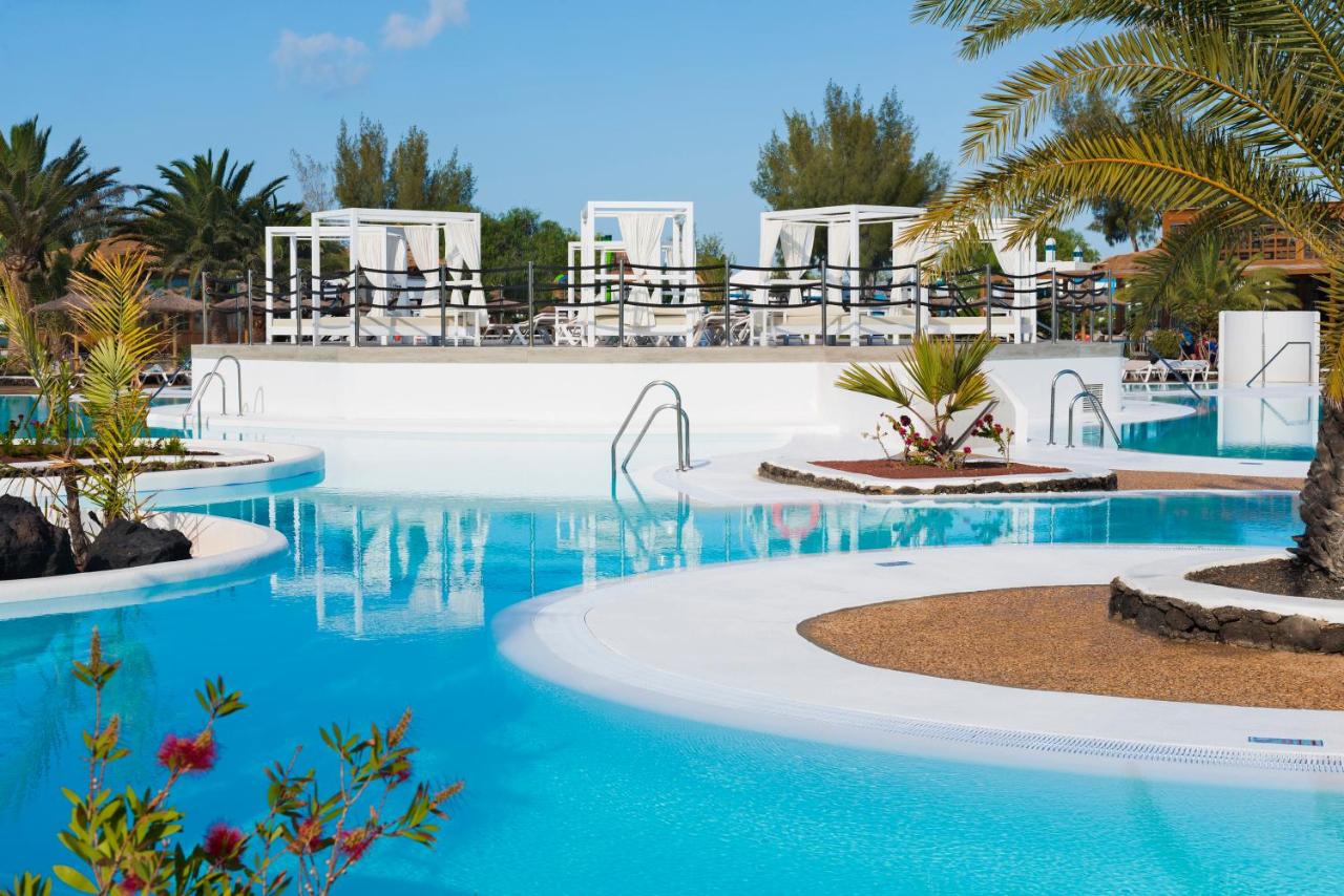 een zwembad in een resort met blauw water en palmbomen bij Elba Lanzarote Royal Village Resort in Playa Blanca