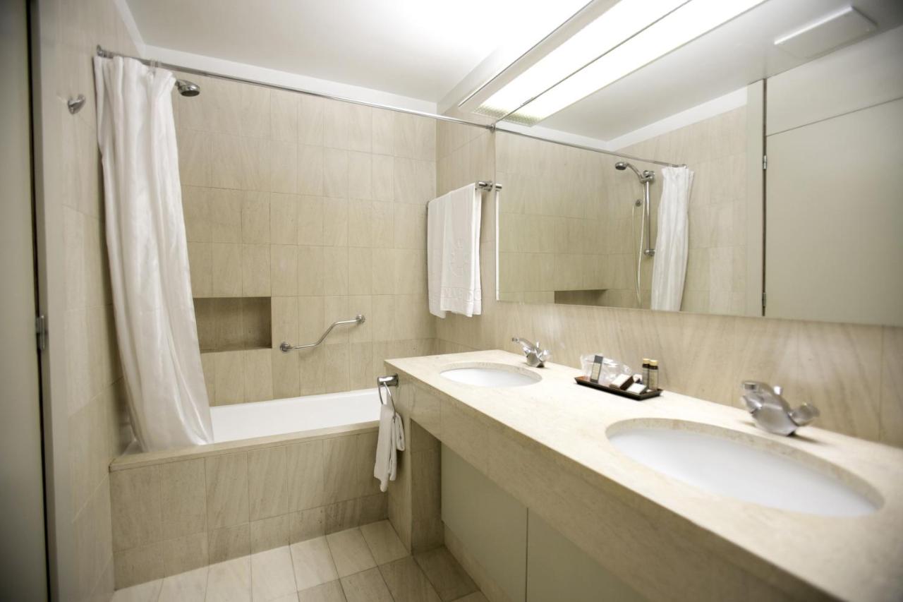 een badkamer met twee wastafels, een spiegel en een badkuip bij Hotel Solverde Spa and Wellness Center in Vila Nova de G
