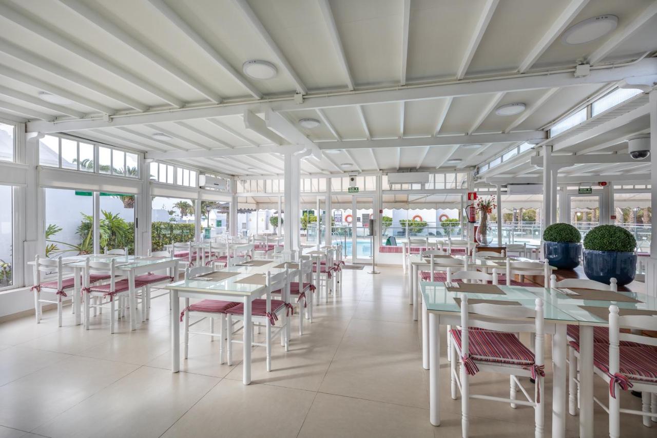 een restaurant met witte tafels en stoelen en ramen bij Apartamentos LIVVO Las Gaviotas in Puerto del Carmen +34 foto's