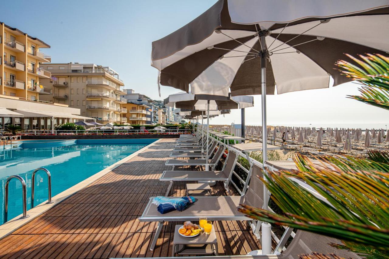 een rij stoelen en parasols naast een zwembad bij Hotel Astor in Lido di Jesolo
