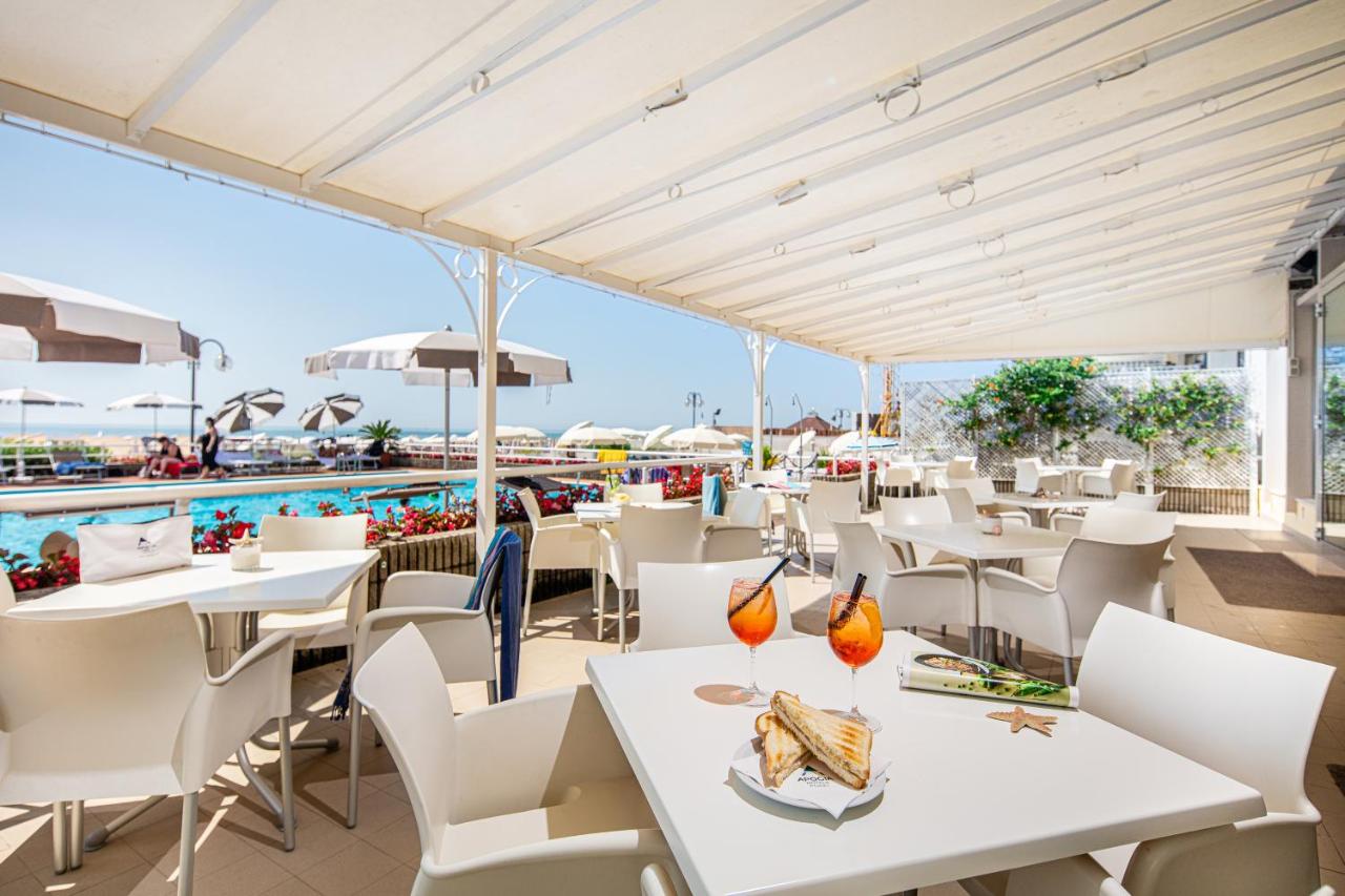 een restaurant met witte tafels en stoelen en een zwembad bij Hotel Astor in Lido di Jesolo