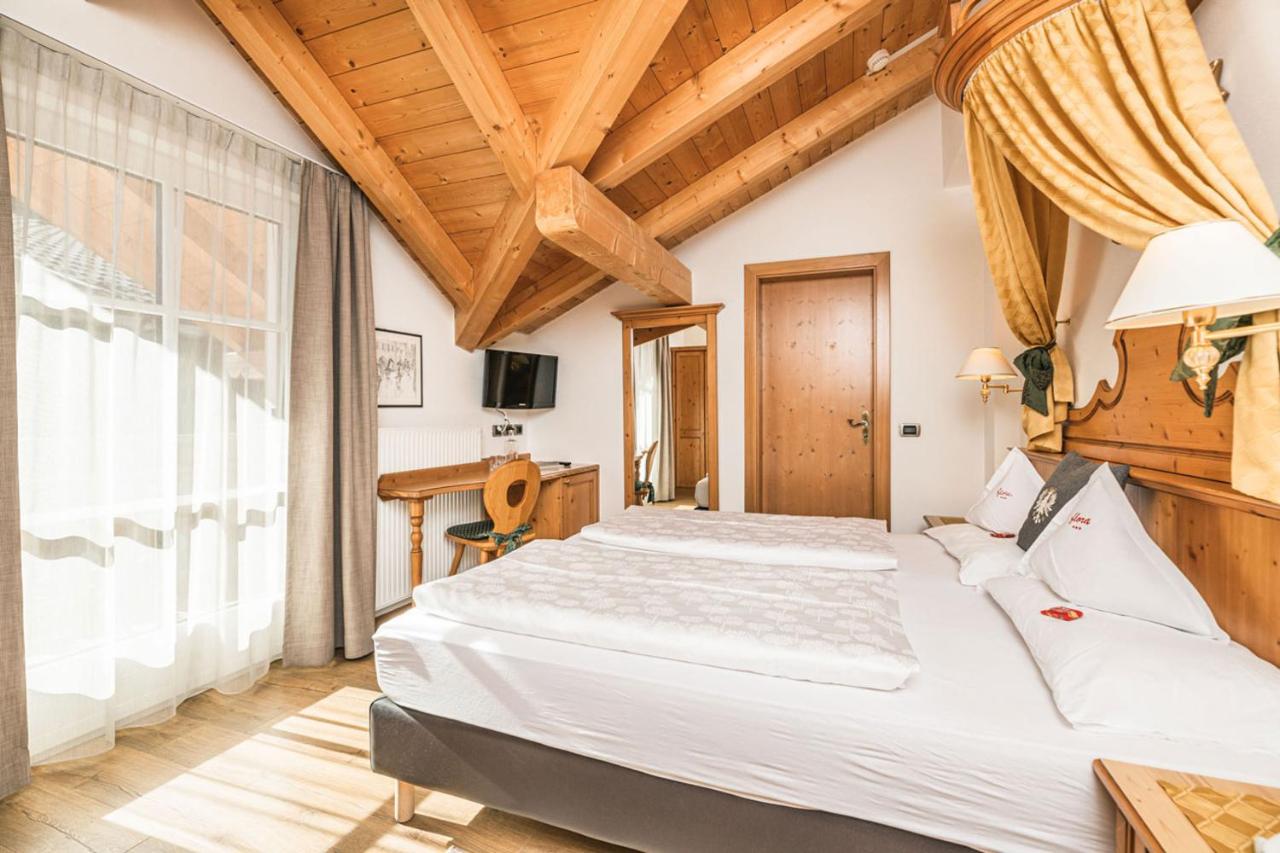 een slaapkamer met twee bedden en een groot raam bij Hotel Flora in Selva di Val Gardena