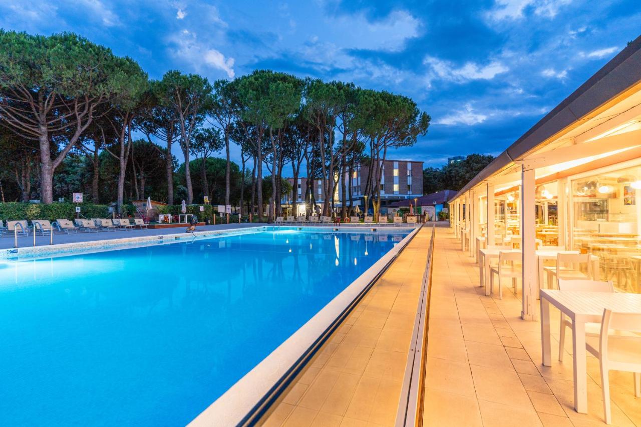 een zwembad met tafels en stoelen naast een gebouw bij Club del Sole Jesolo Family Resort in Lido di Jesolo