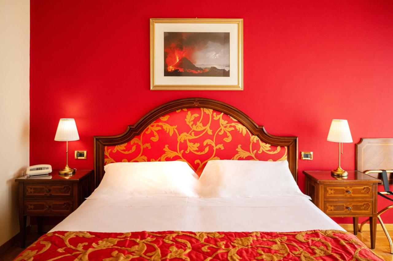 een slaapkamer met een rode muur, een bed en twee lampen bij Hotel Isabella in Taormina