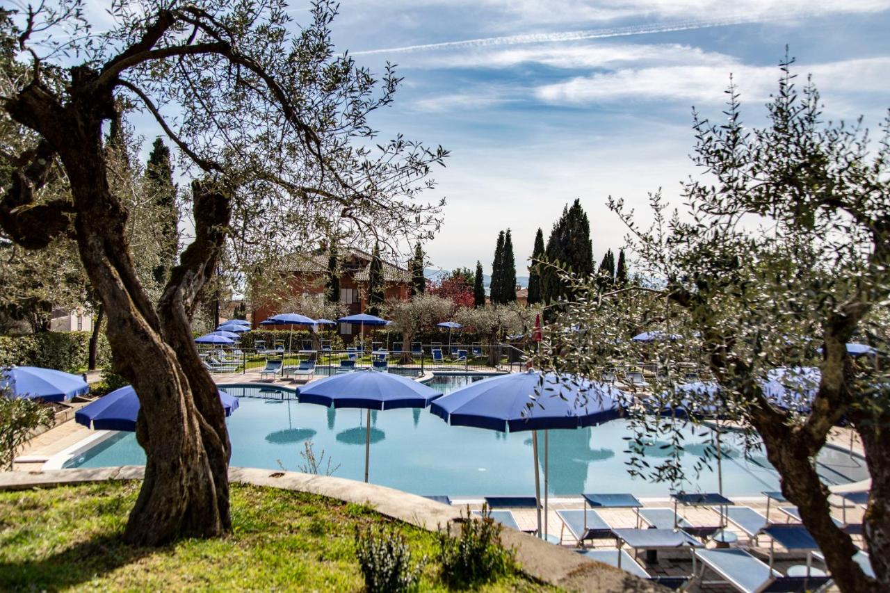 een zwembad met blauwe parasols en ligstoelen bij Hotel Villa Paradiso in Passignano sul Trasimeno