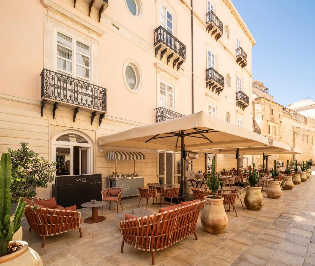 een buitenterras met tafels, stoelen en een parasol bij Palazzo Artemide - VRetreats, an SLH Hotel in Siracusa