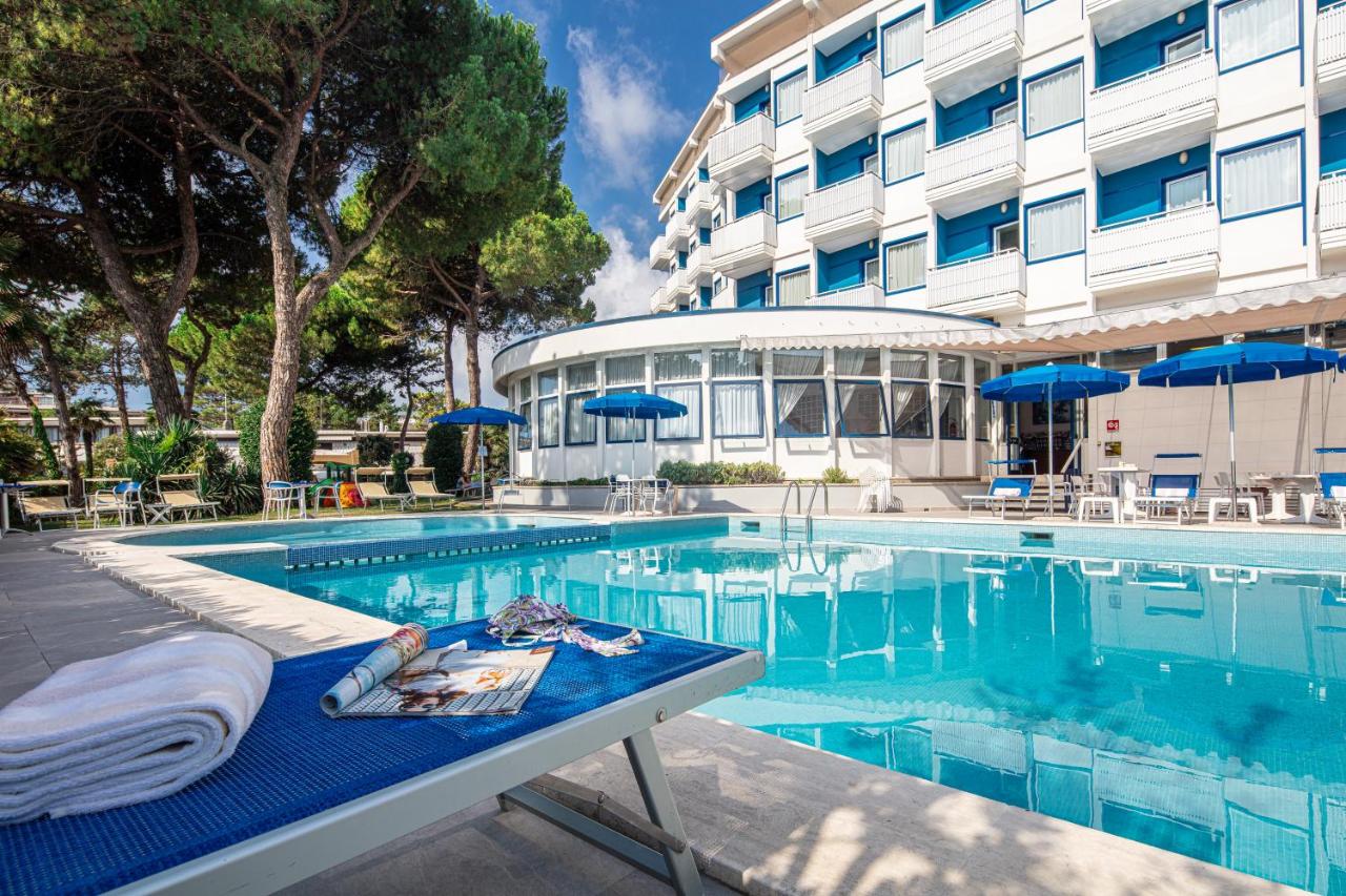 een hotelzwembad met een tafel en blauwe parasols bij Hotel Medusa Splendid in Lignano Sabbiadoro