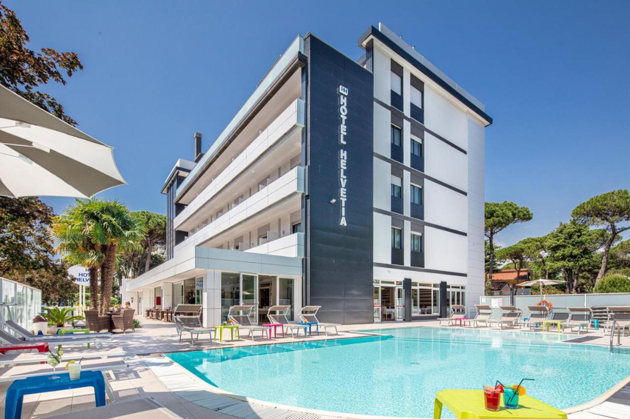 een hotel met een zwembad voor een gebouw bij Hotel Helvetia in Lignano Sabbiadoro