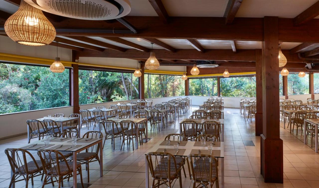 een eetkamer met tafels en stoelen en ramen bij Calaserena Resort in Geremèas
