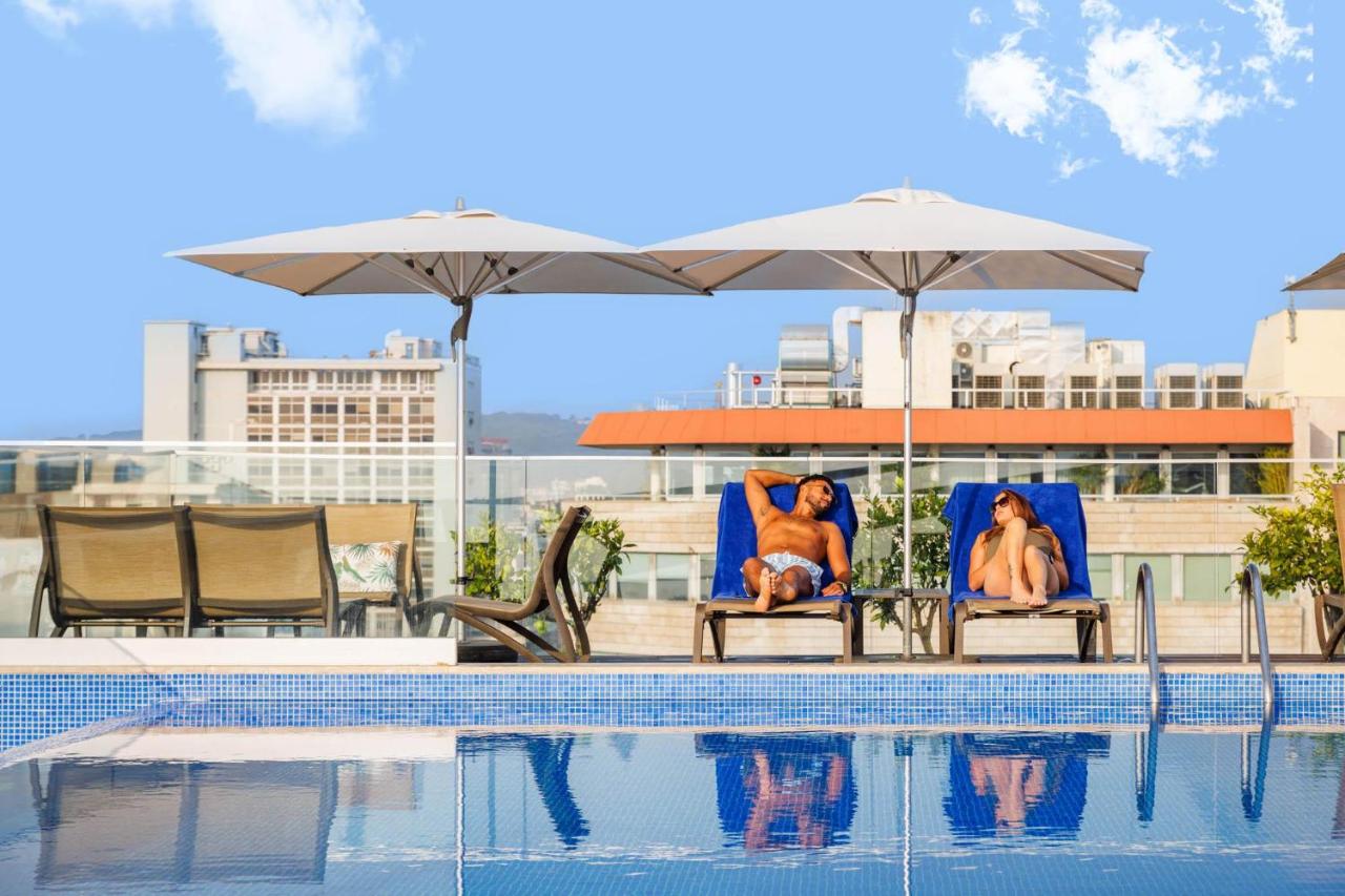 Twee vrouwen zitten op stoelen naast een zwembad. bij Jupiter Lisboa Hotel - Rooftop & Spa in Lissabon