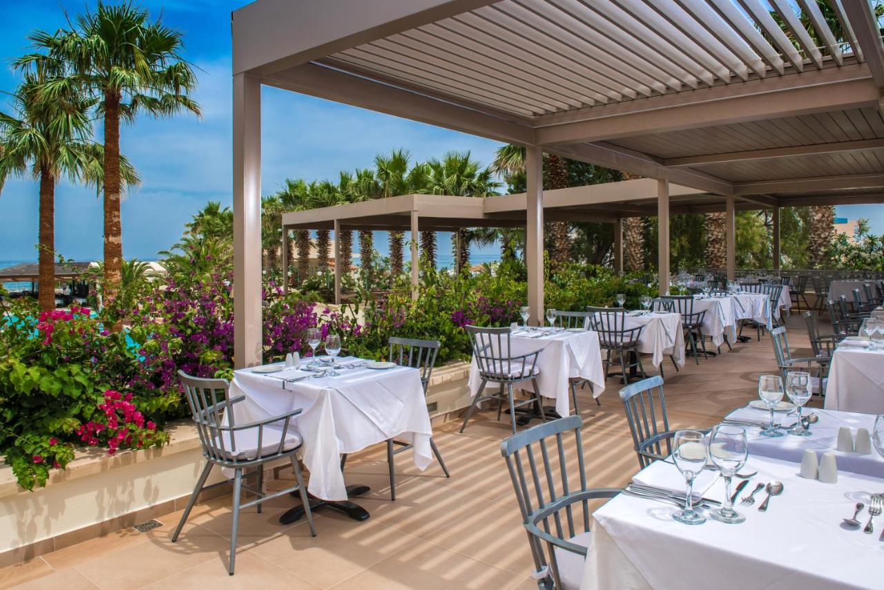 een restaurant met witte tafels en stoelen en palmbomen bij Rethymno Palace in Adelianos Kampos
