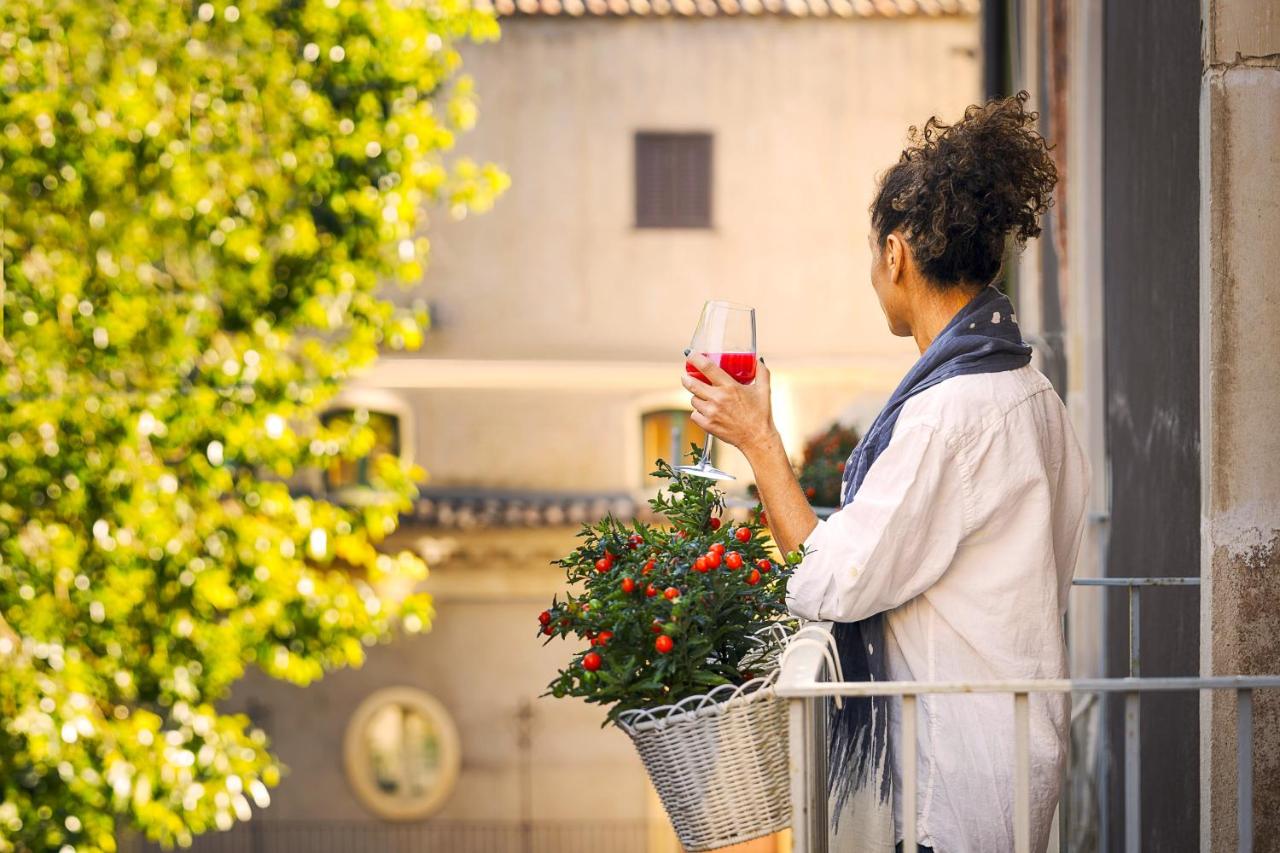 een vrouw staat op een balkon met een glas wijn in haar hand bij B&B Palazzo Cerami in Catania