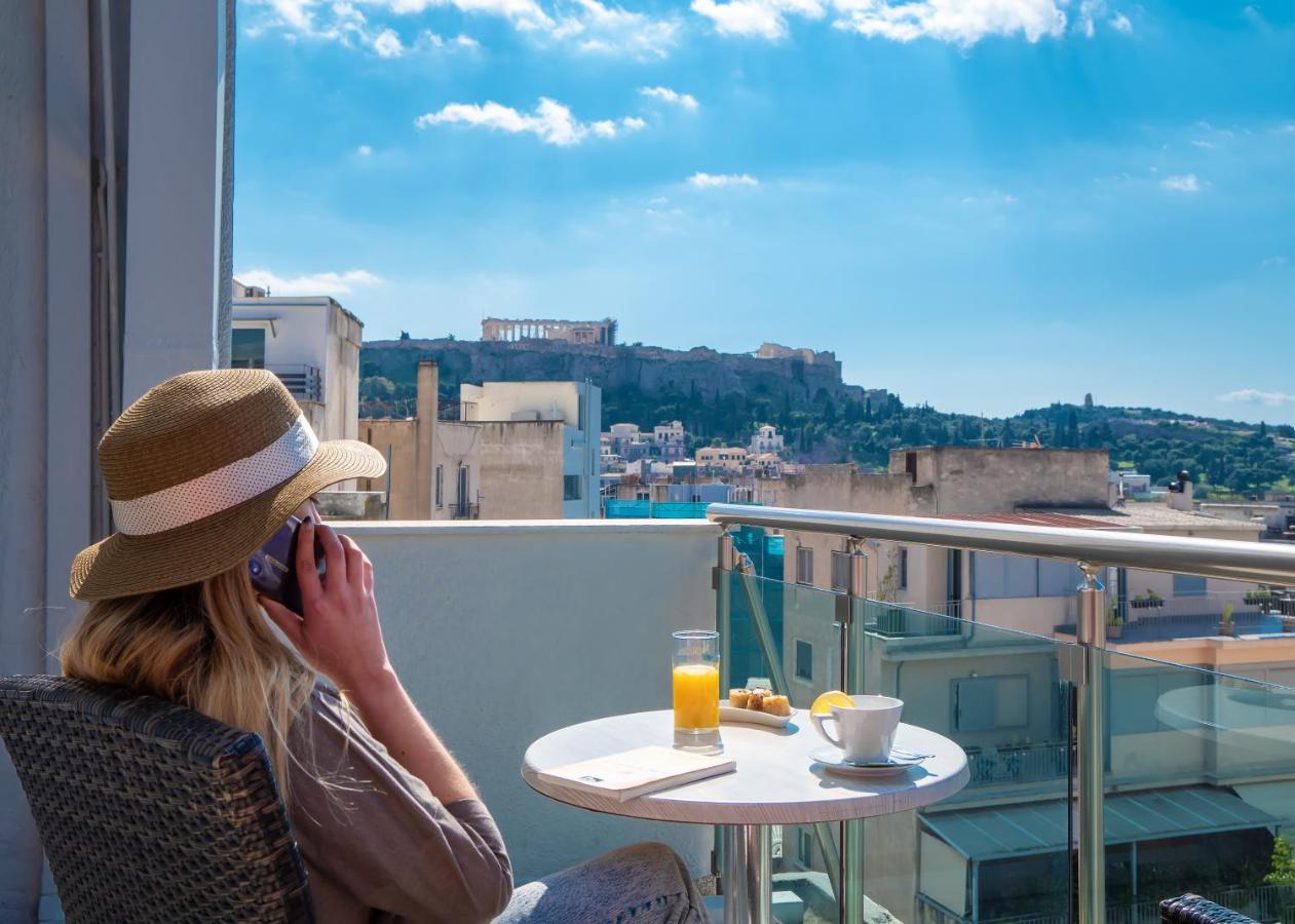 een vrouw zit aan een tafeltje op een balkon en praat aan de telefoon. bij Attalos Hotel in Athene