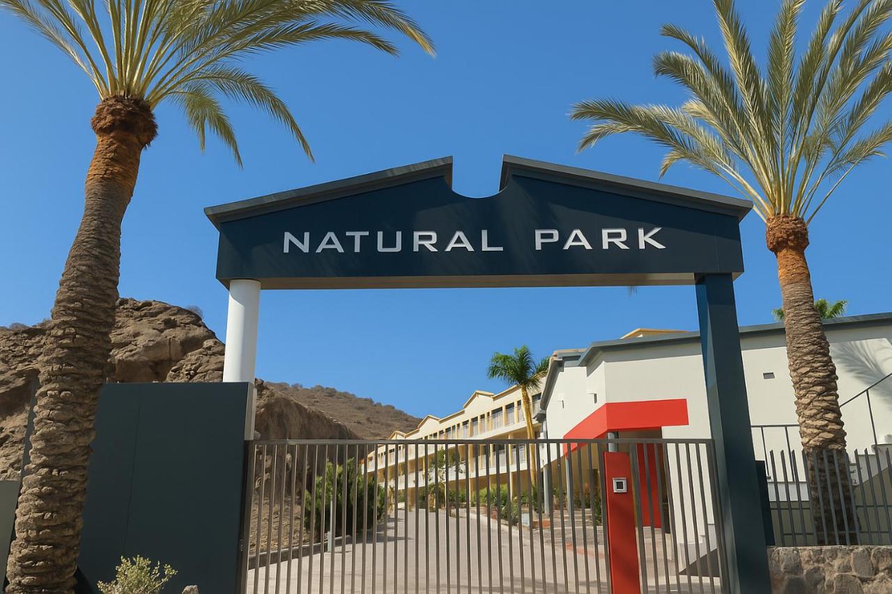 een bord voor een natuurpark met twee palmbomen bij Apartamentos Natural Park in Puerto Rico de Gran Canaria