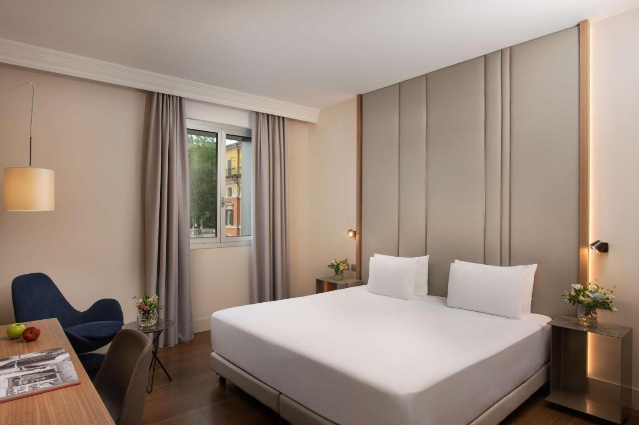 een hotelkamer met een wit bed en een bureau bij NH Bologna De La Gare in Bologna