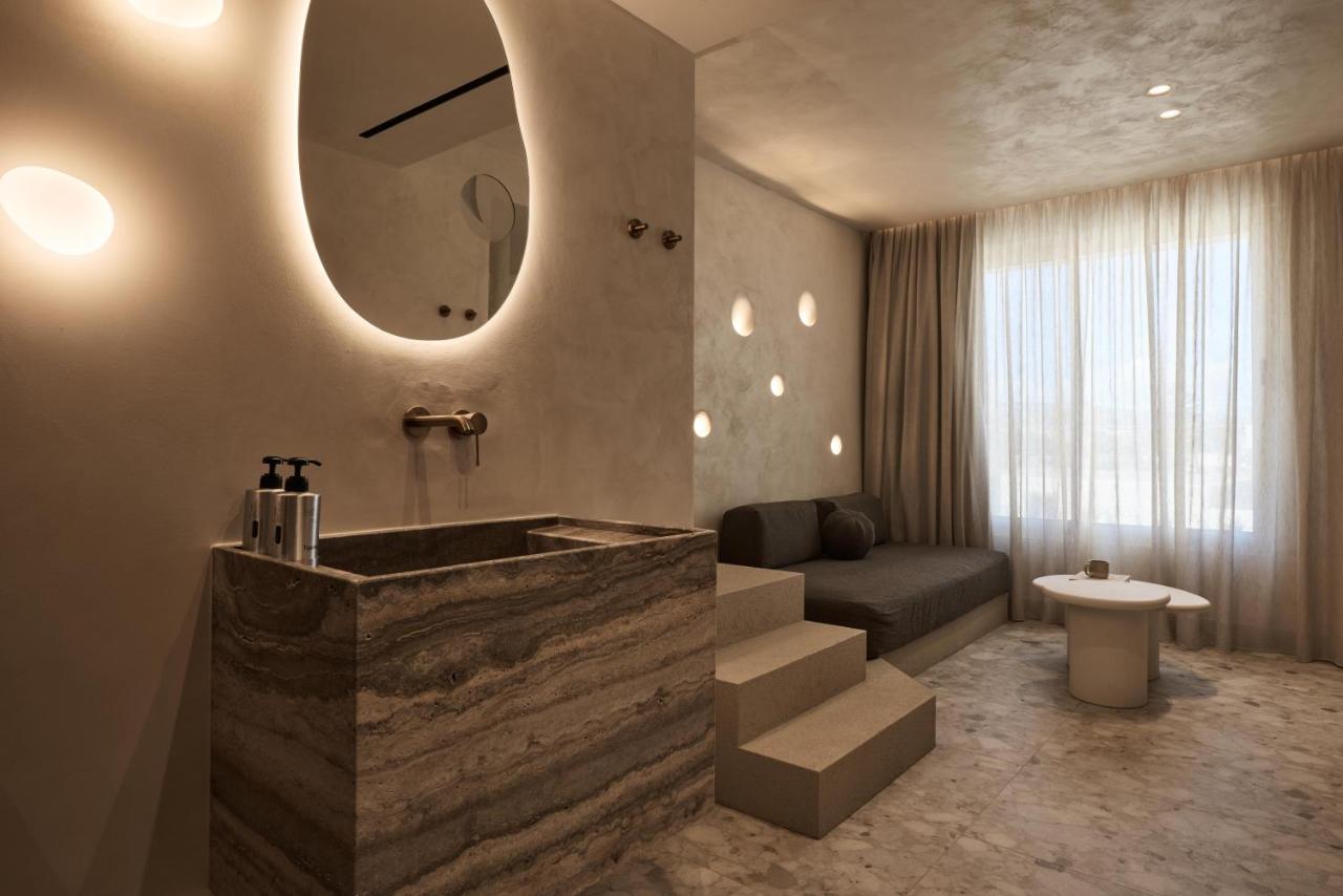 een badkamer met een bad, een bank en een spiegel bij Uzenie All Suites Boutique Resort - Adults Only in Adelianos Kampo