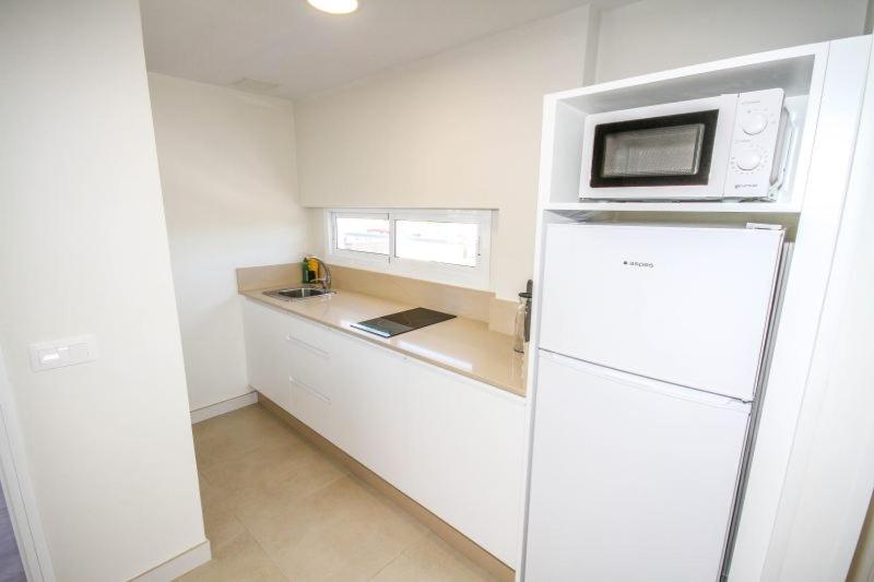 een witte keuken met een magnetron bovenop een koelkast bij New Miami Playa Apartamentos in San Agustin