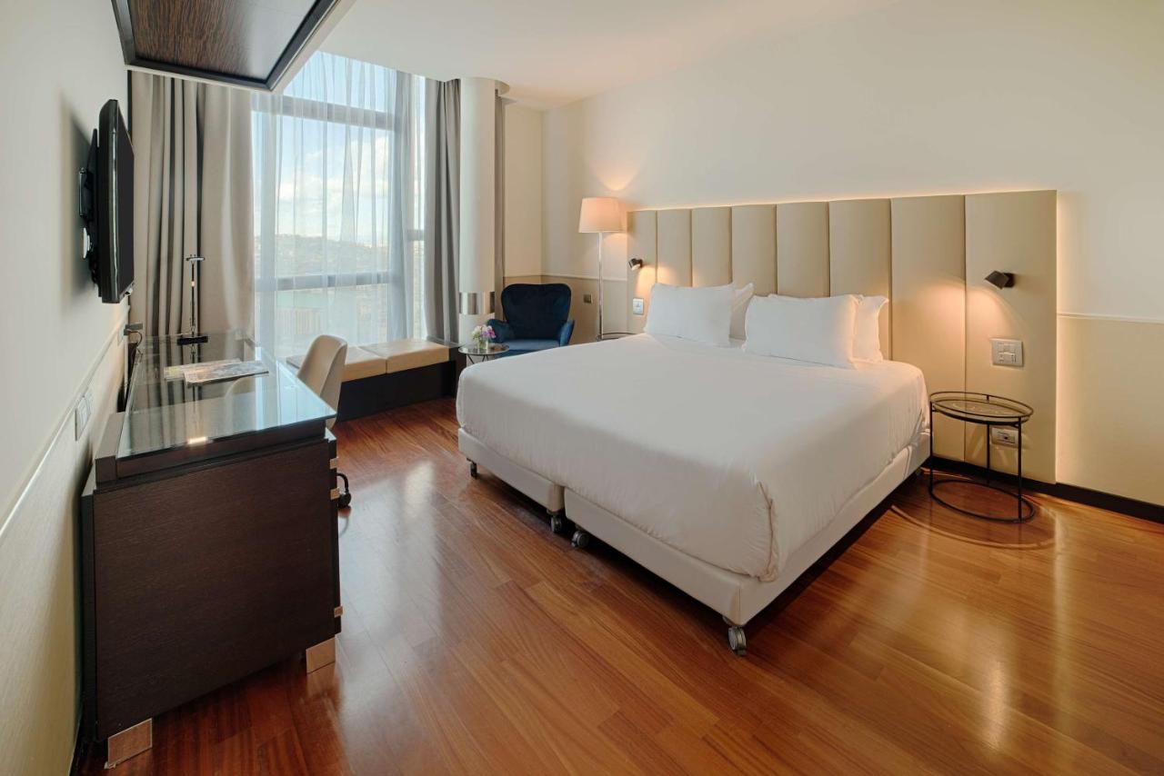 een slaapkamer met een groot wit bed en een raam bij NH Napoli Panorama in Napels