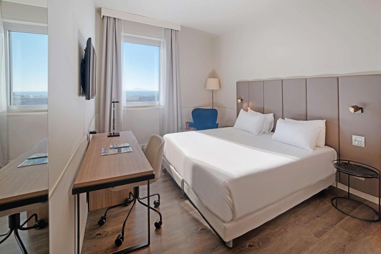 een slaapkamer met een groot wit bed en een bureau bij NH Napoli Panorama in Napels