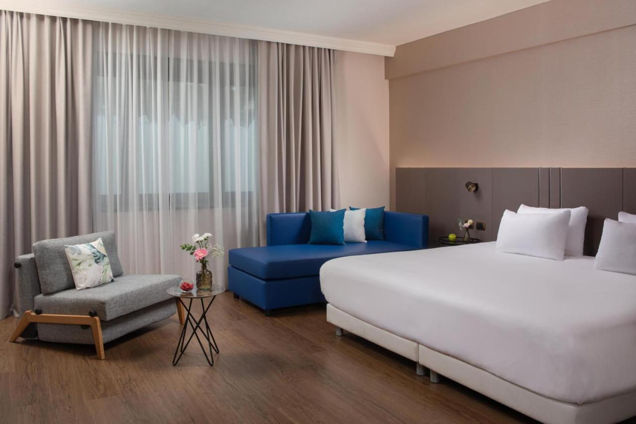 een hotelkamer met een groot bed en een blauwe bank bij NH Roma Villa Carpegna in Rome