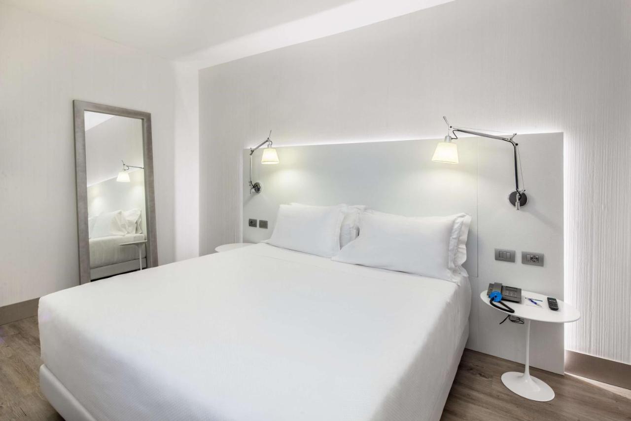 een witte slaapkamer met een groot bed en een spiegel bij NH Milano Congress Centre in Assago