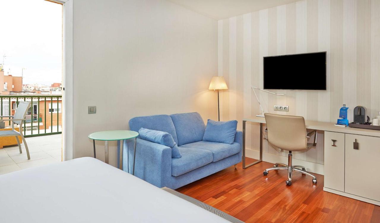 een kamer met een blauwe stoel en een bureau met een tv bij NH Barcelona Les Corts in Barcelona