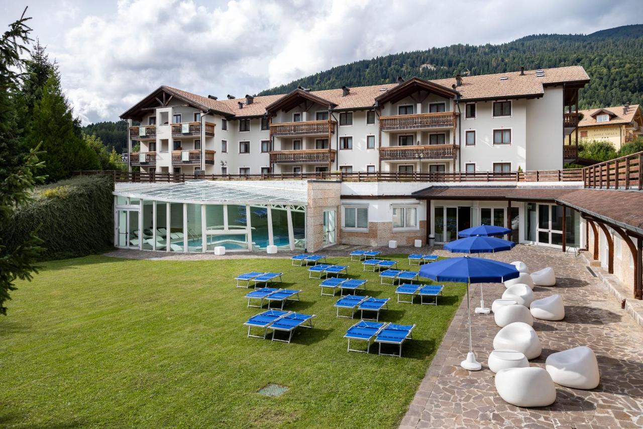 een hotel met blauwe stoelen en parasols op een binnenplaats bij Golf Hotel in Folgaria
