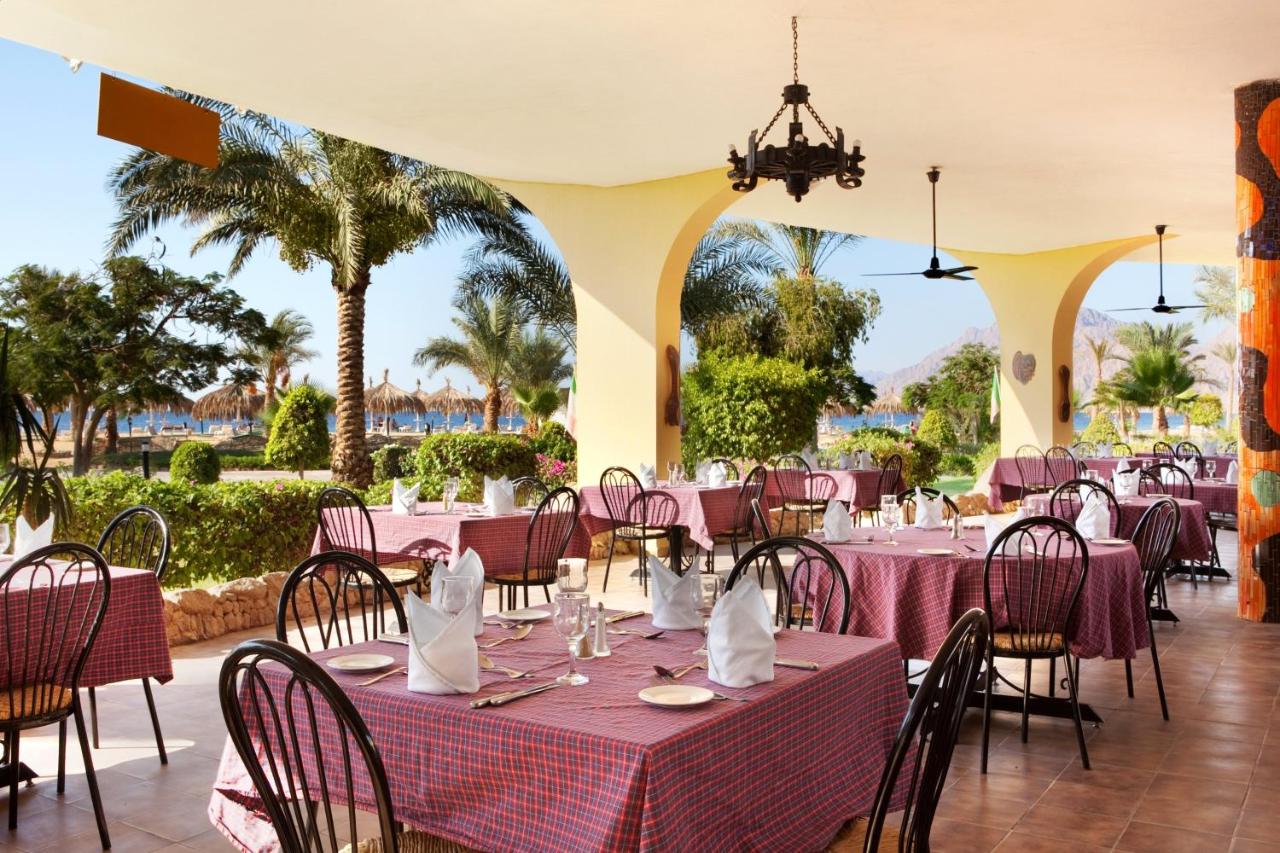 een restaurant met roze tafels en stoelen en palmbomen bij TIME Coral Nuweiba Resort in Nuweiba