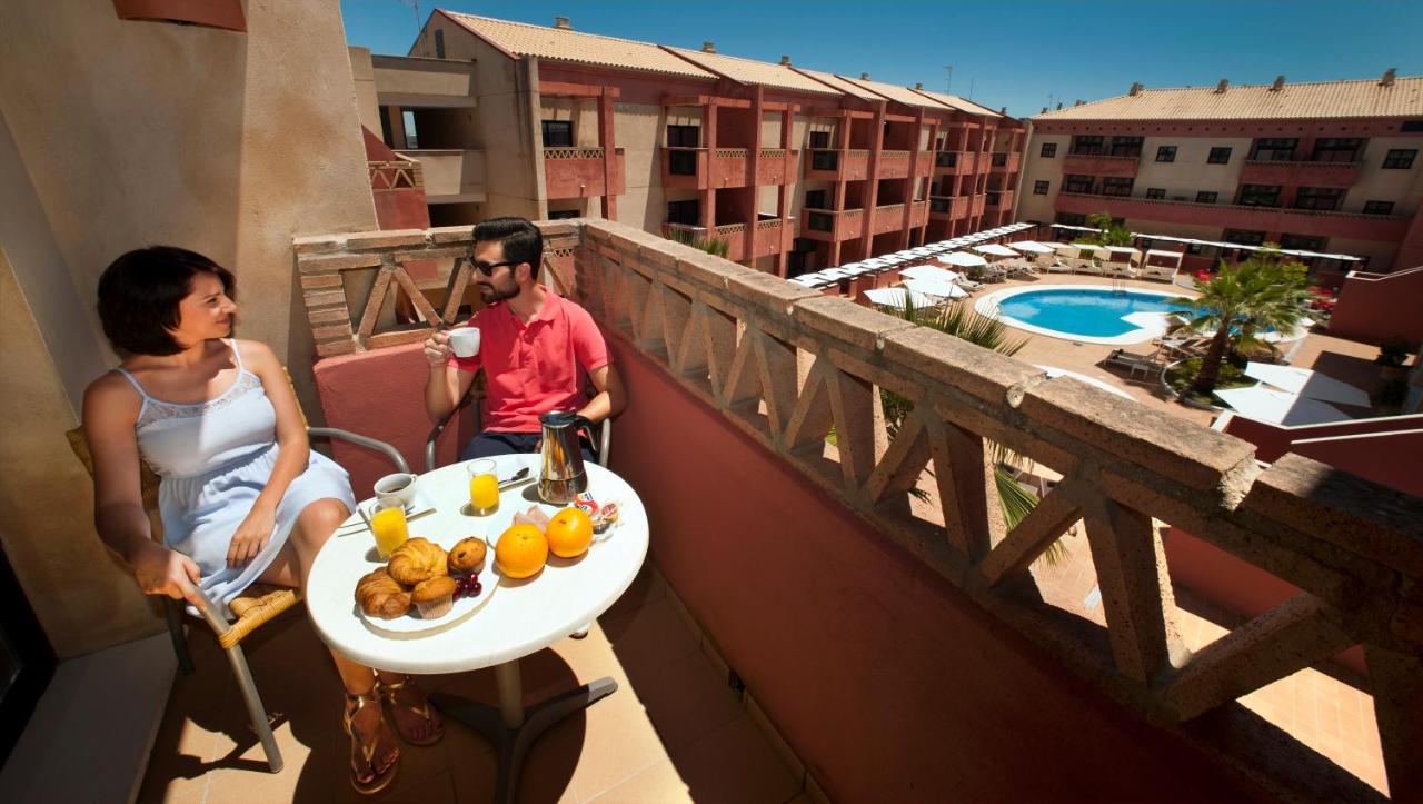 Een man en een vrouw zitten op een balkon met een schaal fruit. bij Leo Punta Umbría - Adults Only in Punta Umbría