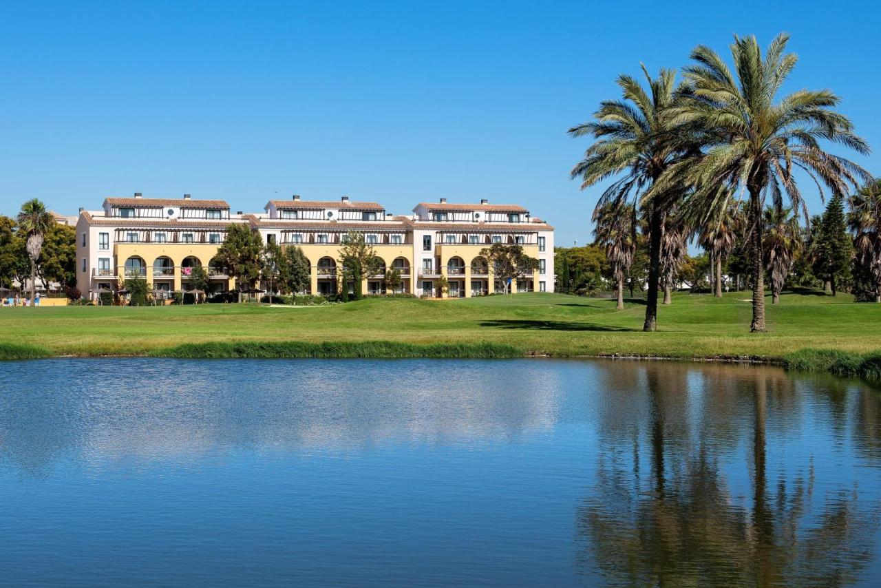 een groot wit gebouw met palmbomen en een vijver bij Barceló Costa Ballena Golf & Spa in Costa Ballena +106 foto's