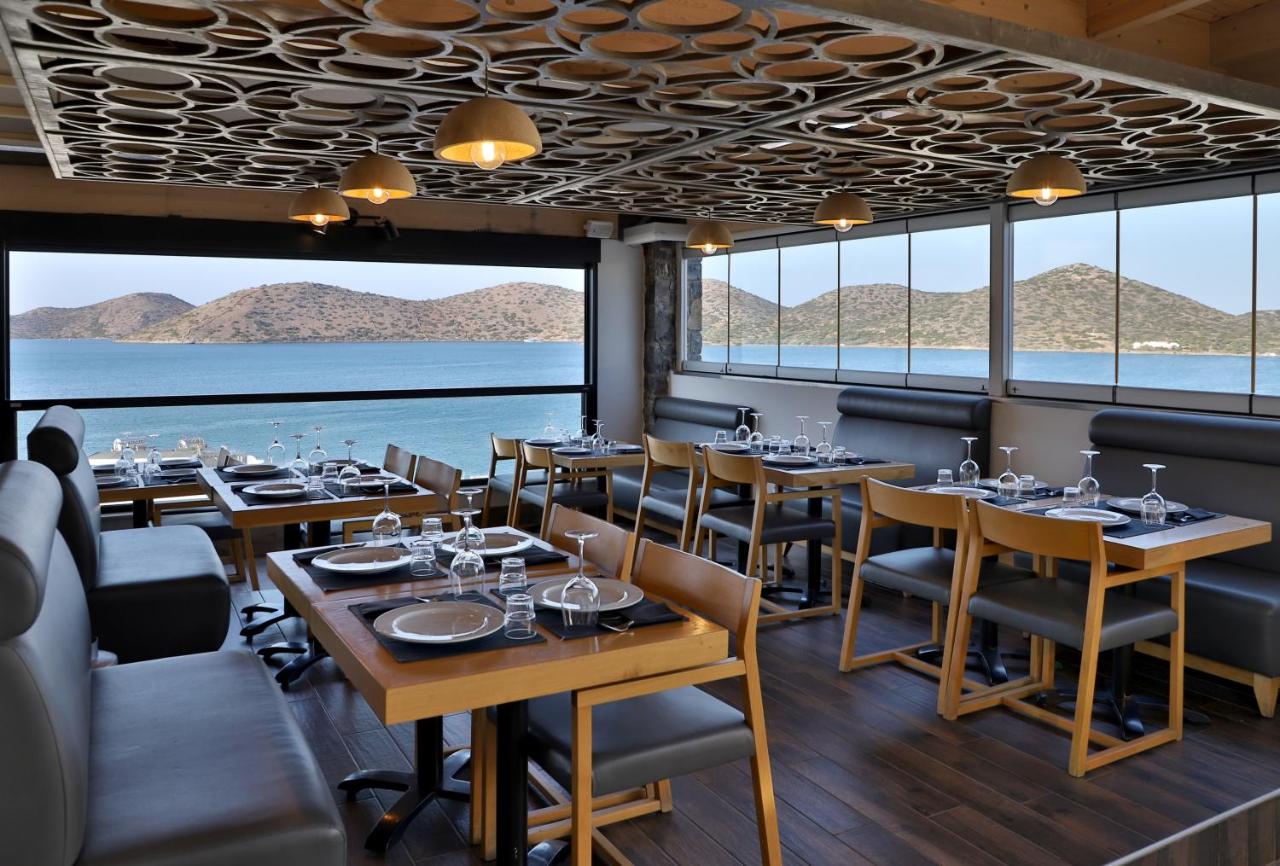 een restaurant met tafels en stoelen en uitzicht op het water bij Elounda Orama by GHH in Elounda