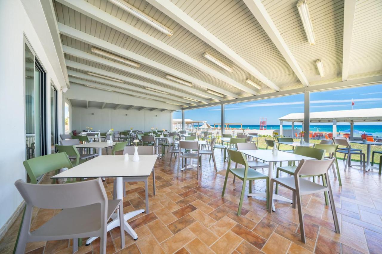 een restaurant met tafels en stoelen en uitzicht op de oceaan bij Adele Beach Hotel in Adelianos Kampos
