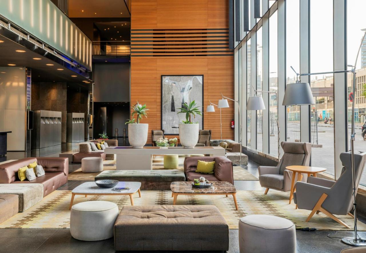 een woonkamer met banken, tafels en ramen bij Leonardo Royal Hotel Barcelona Forum in Barcelona