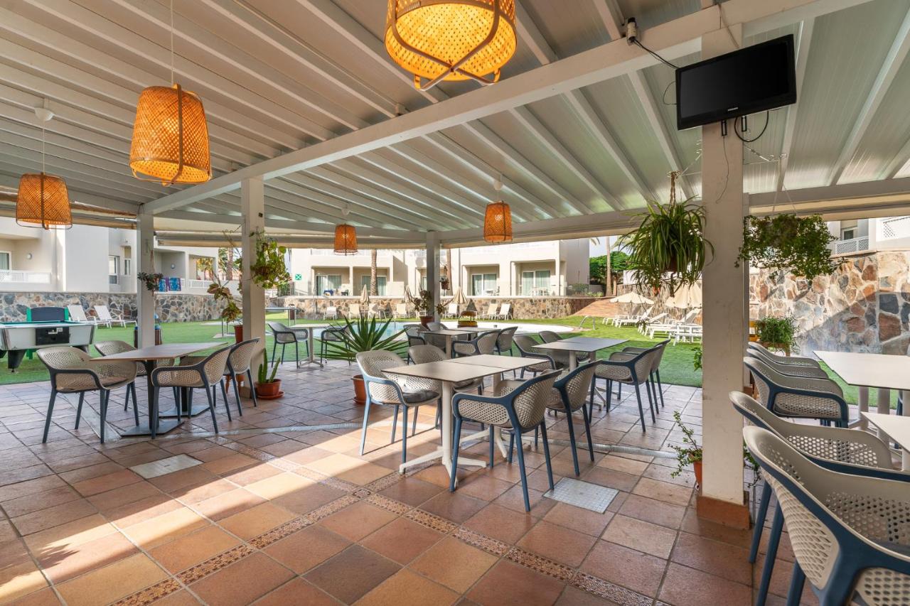 een terras met tafels en stoelen en een flatscreen-tv bij Apartamentos LIVVO Koala Garden in Maspalomas