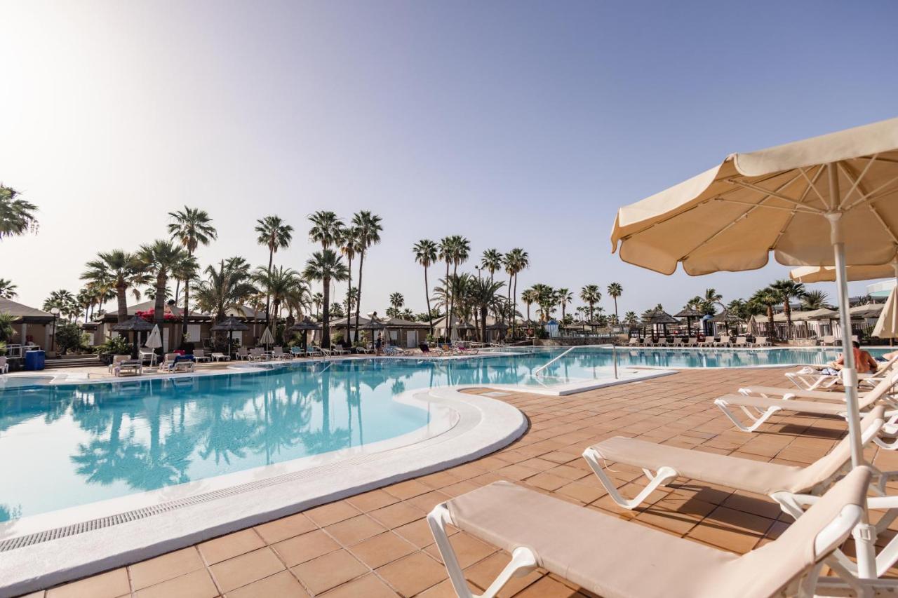 een zwembad bij een resort met ligstoelen en een parasol bij Caybeach Princess in Maspalomas