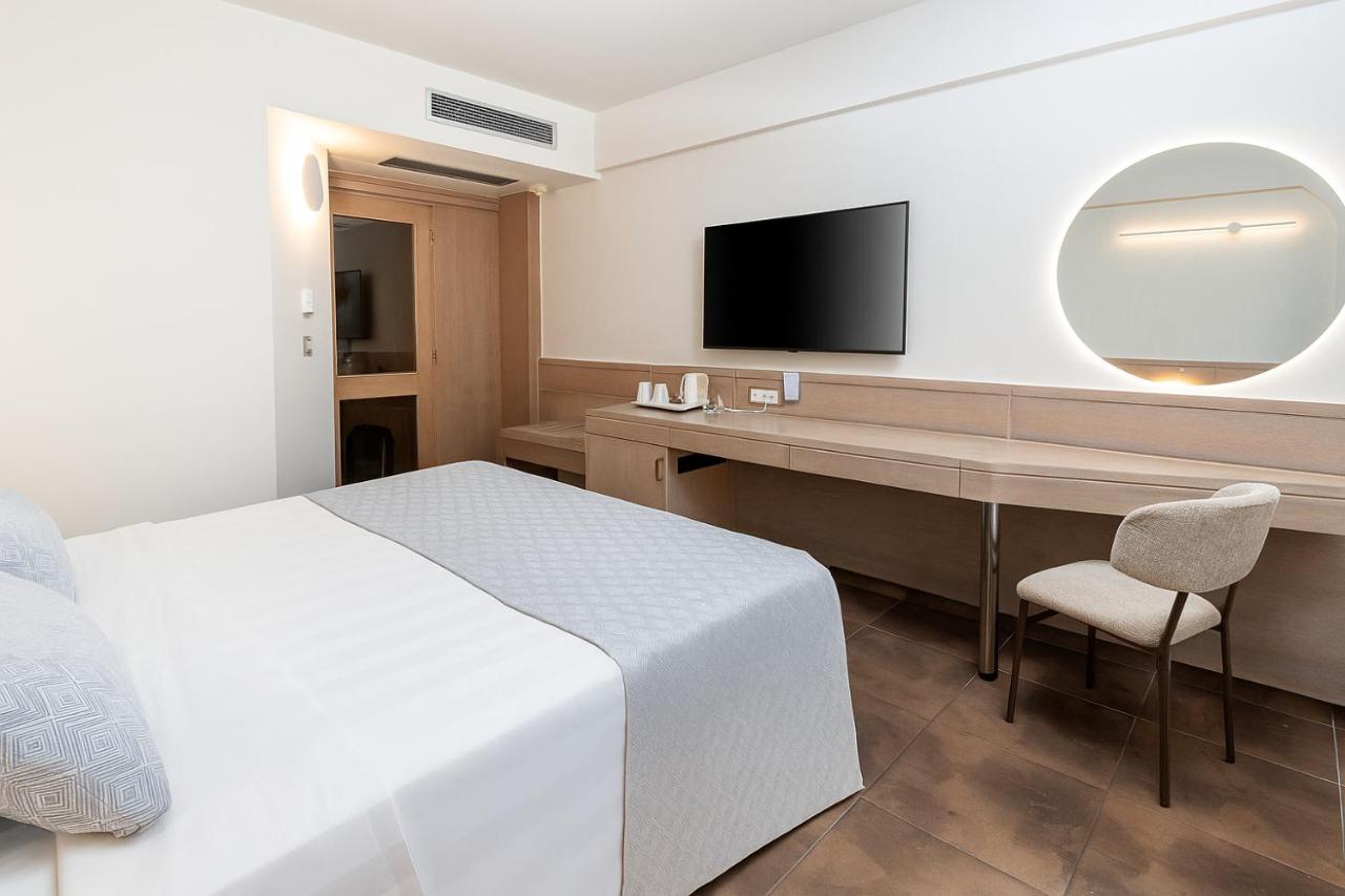 een slaapkamer met een bed en een bureau met een televisie bij Thalassa Beach Resort & Spa (Adults Only) in Agia Marina 
