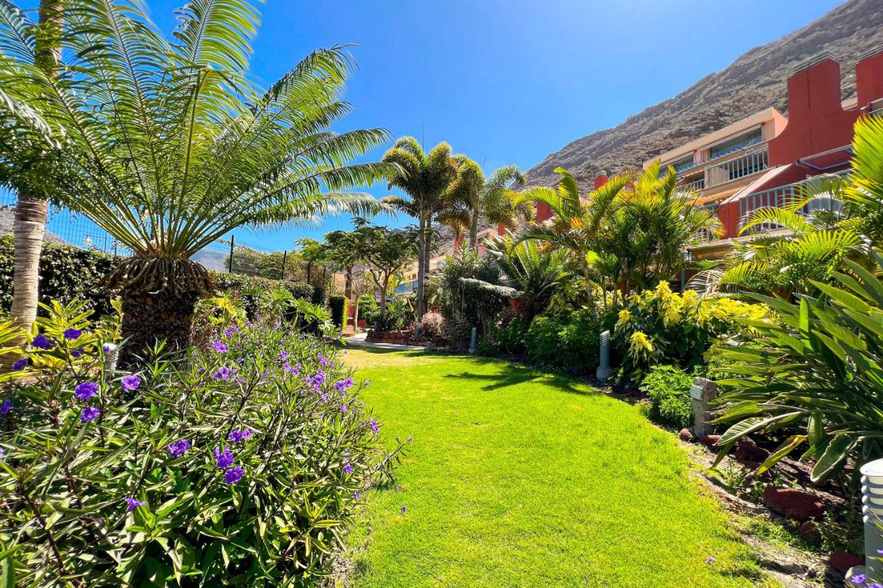 een tuin met palmbomen en bloemen voor een gebouw bij Apartamentos Cordial Mogán Valle in Puerto de Mogán