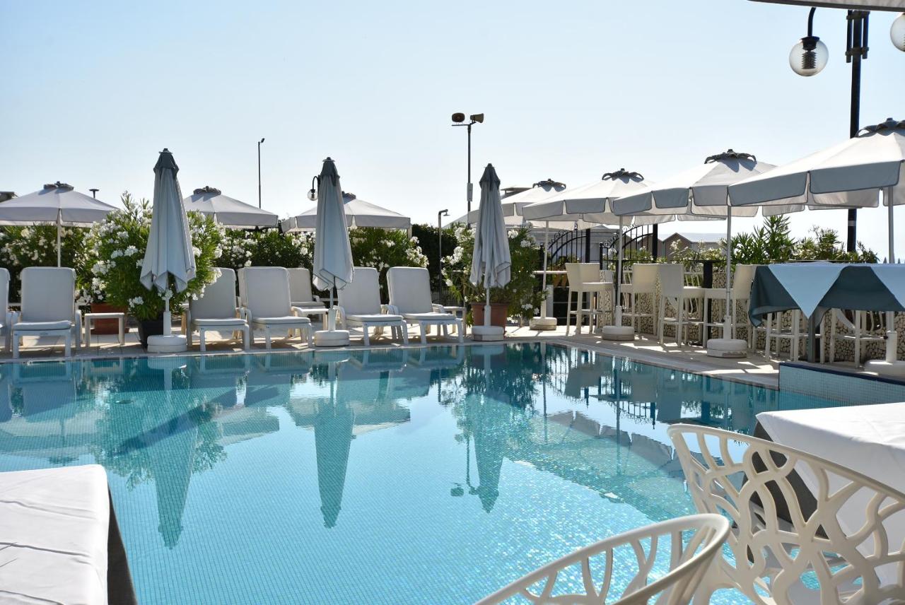 een groot zwembad met witte stoelen en parasols bij Hotel Oxford in Lido di Jesolo