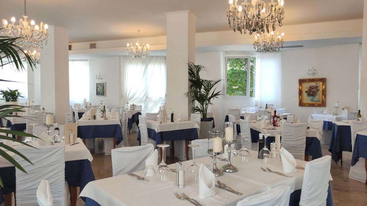 een eetkamer met witte tafels en stoelen en kroonluchters bij Hotel Oxford in Lido di Jesolo