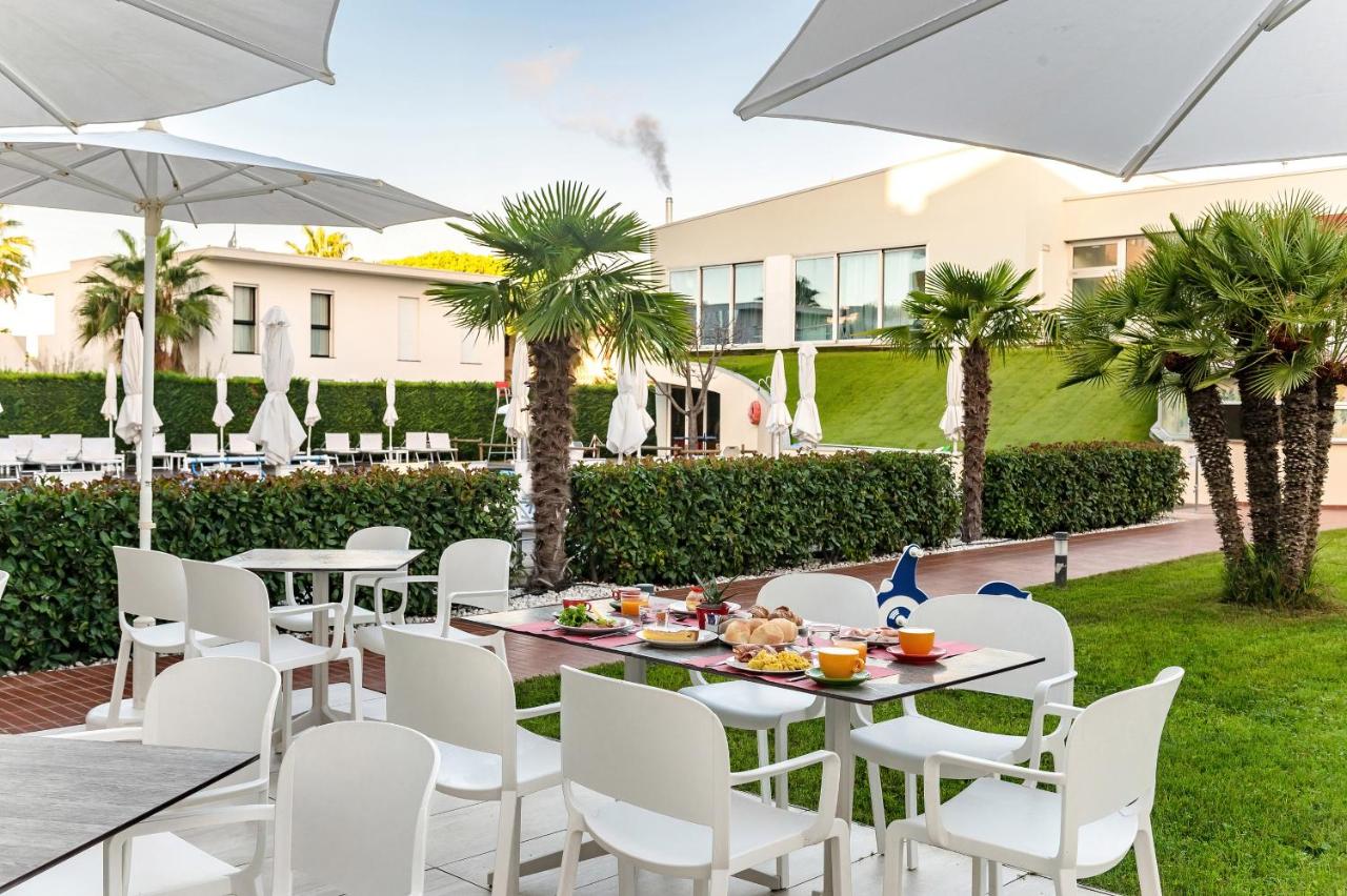 een terras met witte stoelen en tafels en parasols bij Domino Suite Hotel & Residence in Lido di Jesolo