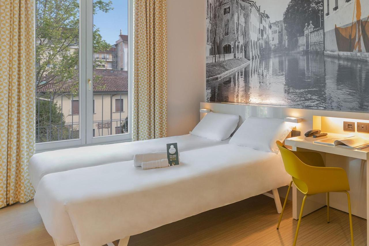 een slaapkamer met een bed, een bureau en een groot raam bij B&B Hotel Treviso in Treviso