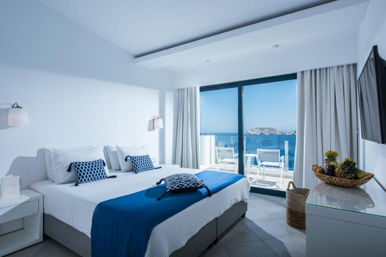 een witte slaapkamer met een bed en een groot raam bij Peninsula Resort & Spa in Agia Pelagia